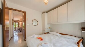 A hotel room with a bed, a mirror, a wooden headboard, a bedside table, and a view of the dining area.