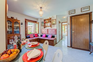 A dining area with a table set for four, a wooden cabinet with glass doors, a bench with cushions, and a wooden door.