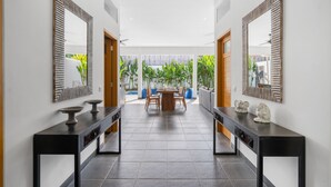 A modern hallway with two black console tables, each with a mirror and decorative items. The hallway leads to a dining area with a wooden table and chairs. - Pasha Villa by Betterplace (Kerobokan)