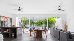 A modern interior with a dining area, a sofa, ceiling fans, and a view of a pool and greenery. - Pasha Villa by Betterplace (Kerobokan)