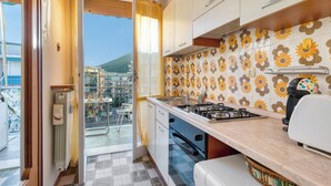 A kitchen with a gas stove, a coffee maker, and a view of the outside. - Il Rifugio - Town Center Apartment with Balcony, Borghetto Santo Spirito, Italy (Borghetto Santo Spirito)