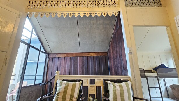 Una habitación con techo de madera, un banco con cojines a rayas, una mesita con un cactus y una ventana que da a vistas del exterior.