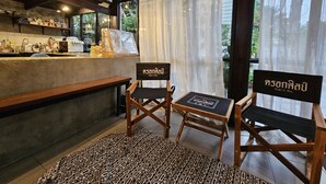 Un café acogedor con sillas de madera, una barra con utensilios de cocina y vistas a través de cortinas traslúcidas.