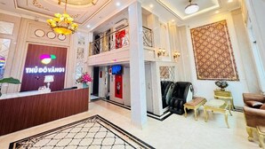 A hotel lobby with a reception desk, a chandelier, a massage chair, and a patterned wall. - Thu Do Vang Hotel Ha Dong By Bay Luxury (Hanoi)