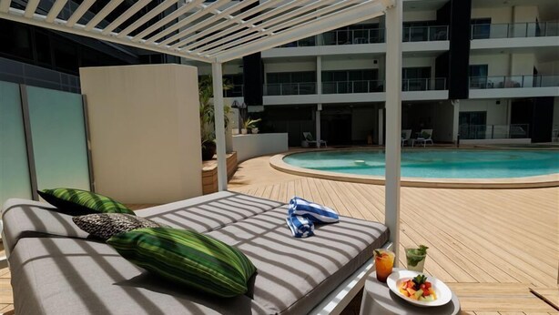 A poolside lounge area with a sunbed, a drink, and a plate of fruit. - Harbour View Apartment on 11th floor | King Bed (Darwin City)
