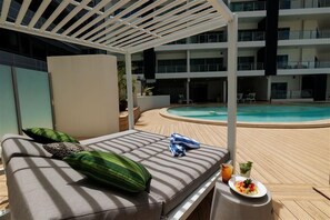 A poolside lounge area with a sunbed, a drink, and a plate of fruit. - Harbour View Apartment on 11th floor | King Bed (Darwin City)