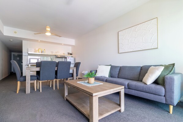 Ett modernt vardagsrum med en grå soffa, ett soffbord, en matplats med stolar och ett kök i bakgrunden.