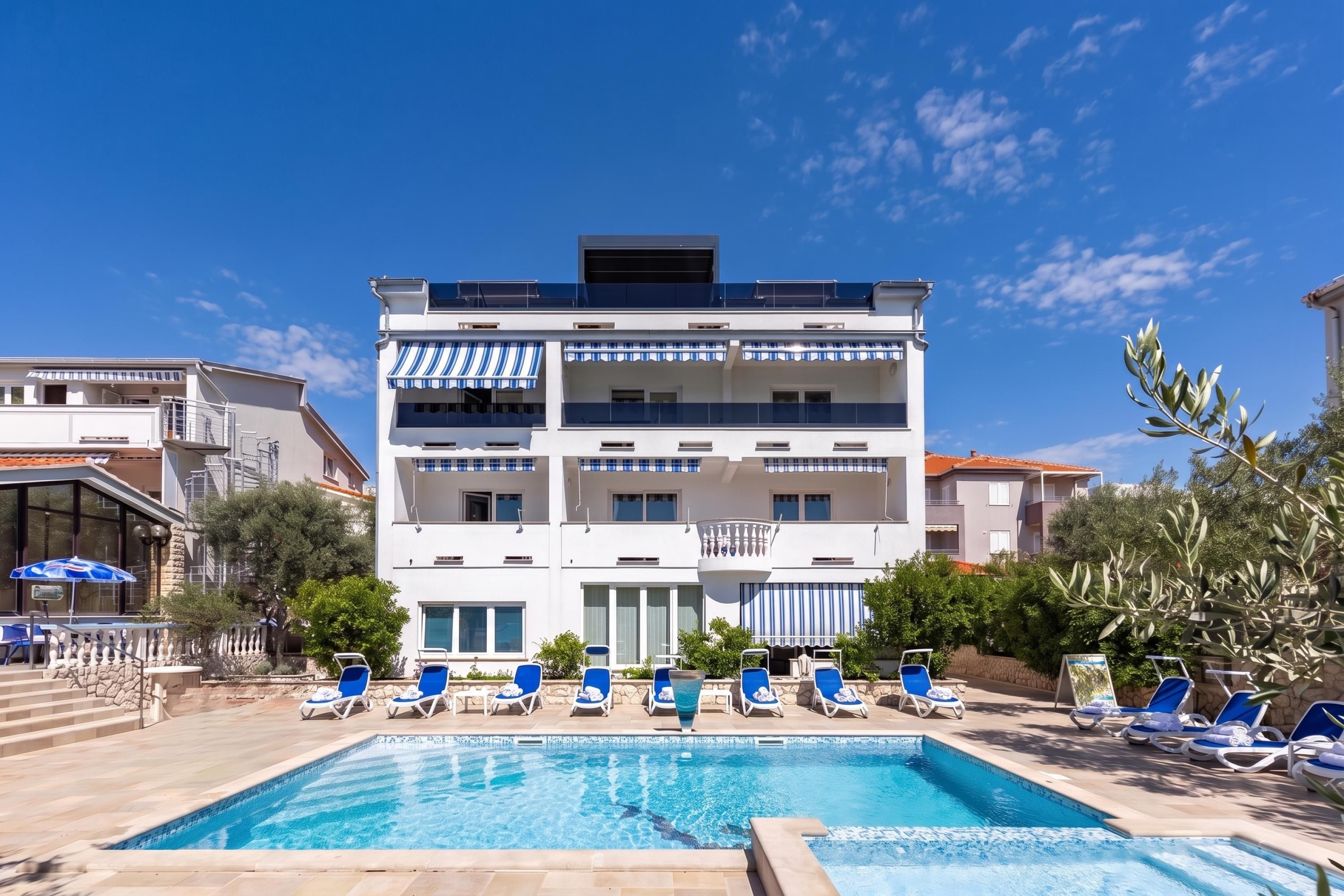 Ett hotell med flera våningar, en swimmingpool och solstolar.