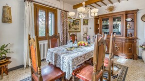 A dining room with a wooden table set for four, surrounded by chairs. There is a chandelier above the table, and a cabinet with glass doors to the right. - Villa Paola Private Pool Gym in Chianti (Montespertoli)