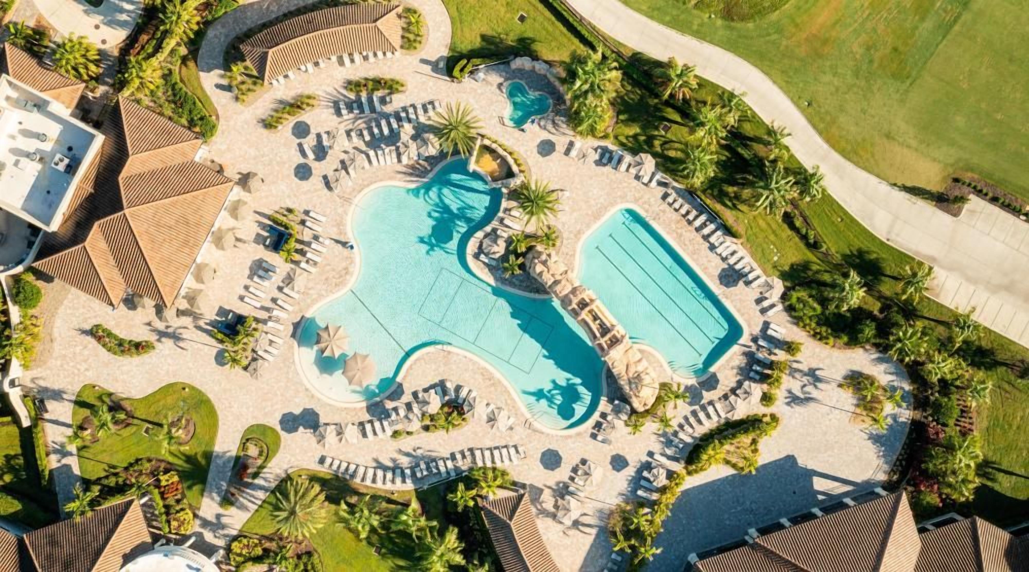 Vue aérienne d’un complexe hôtelier doté de plusieurs piscines, de chaises longues et de palmiers.