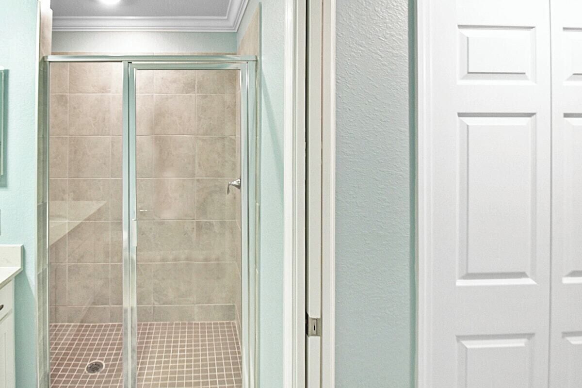 Un baño con cabina de ducha de vidrio, una puerta blanca y piso de baldosas.