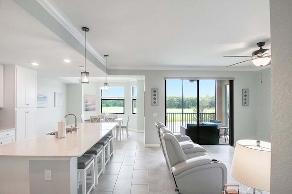 Uma cozinha moderna com uma ilha central, uma sala de jantar com mesa e cadeiras, e um espaço de estar com sofá e luminária.
