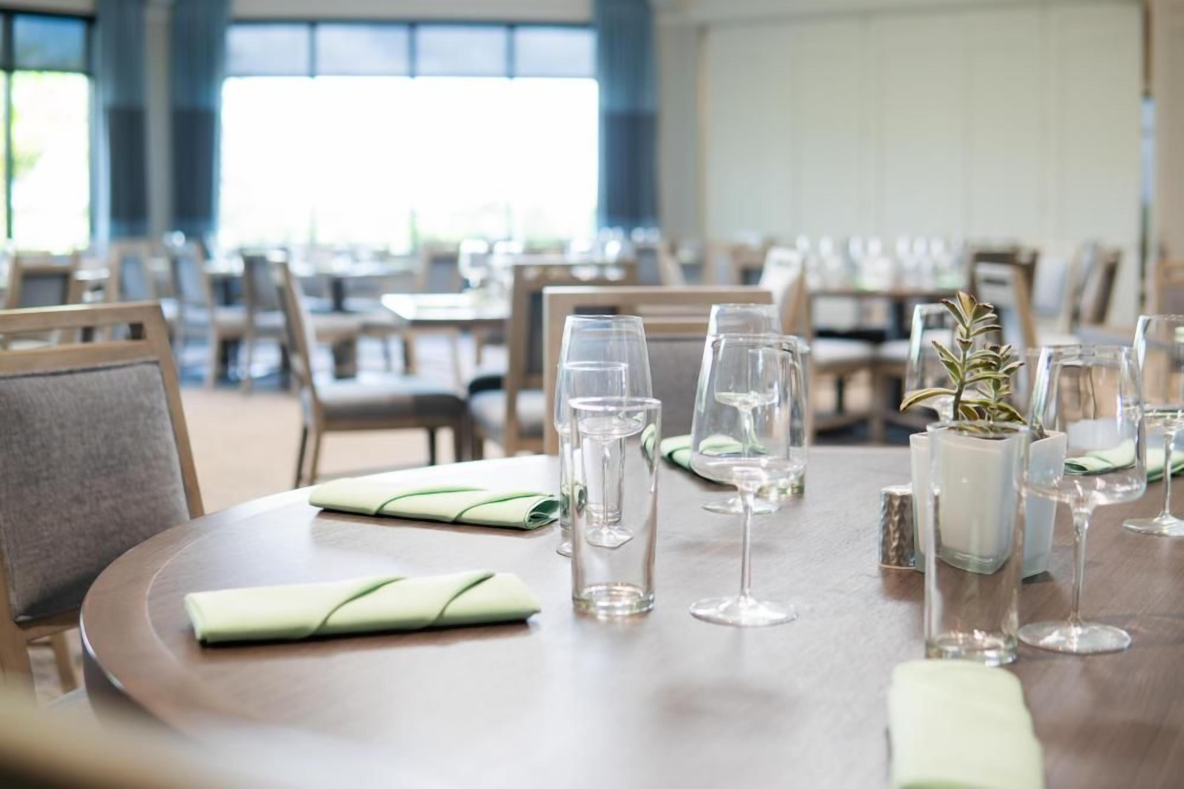 Un espace repas avec des tables rondes, disposées et mises avec des verres à eau, des verres à vin et des serviettes pliées.