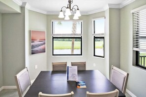 Un comedor con una mesa oscura, cuatro sillas, una araña y ventanas grandes con persianas.