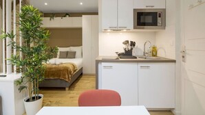 Une petite chambre comprenant un lit, un coin cuisine et une plante en pot.
