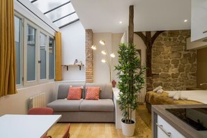 A compact living space with a sofa, a dining table, a potted plant, and a bed. - Typical Parisian Studio in Le Marais#4 pers (Paris)