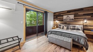 A modern bedroom with a large bed, a bench, a wooden slatted wall, and a view through a sliding door. - The Mountain Retreat - Loon Mtn - Pools - Views - Shuttle Service (Lincoln)