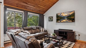A living room with a leather sofa, a coffee table, a TV stand, and a painting on the wall. - The Mountain Retreat - Loon Mtn - Pools - Views - Shuttle Service (Lincoln)