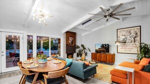 A spacious living room with a dining area, a ceiling fan, and a fireplace. - Luxury Escapade w/ Pool, Hot Tub & Mountain Views (Palm Springs)