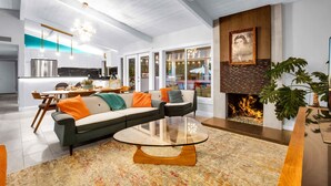 A modern living room with a sectional sofa, a glass coffee table, a fireplace, and a kitchen in the background. - Luxury Escapade w/ Pool, Hot Tub & Mountain Views (Palm Springs)