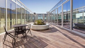 A modern outdoor terrace with glass walls, a wooden deck, and a central planter with plants. - Modern 1B1B Artist APT * WFH Study (Melbourne)