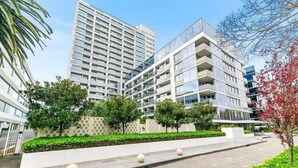 A modern multi-story building with balconies, surrounded by greenery and a paved walkway. - Modern 1B1B Artist APT * WFH Study (Melbourne)