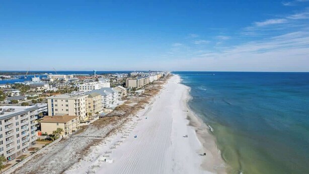 A coastal cityscape with a long sandy beach, beachfront buildings, and a clear blue sky.