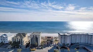 A beachfront hotel with multiple buildings, a parking area, and a view of the ocean.