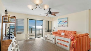 A spacious living room with a wooden floor, a white sofa, a dining table, and a ceiling fan.