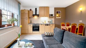 Une cuisine compacte équipée d’un four à micro-ondes, d’un four et de meubles en bois. On y trouve un coin repas avec une table et des chaises, ainsi qu’un canapé dans le salon.