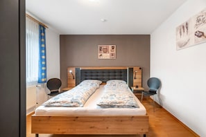 Una camera da letto con un letto di legno, due sedie, un comodino e un'opera d'arte appesa al muro.