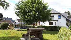 Un parc avec un banc, un arbre et des maisons en arrière-plan.