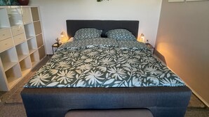 A bedroom with a large bed, bedside tables, a hanging plant, and a bench. - Holiday Apartment "Am Conradhof" with Private Terrace and Wi-Fi (Goch - Pfalzdorf)