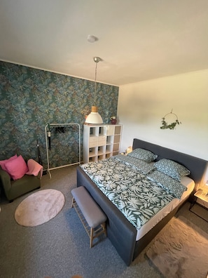 Un dormitorio con cama, un banco, un aparador, una lámpara colgante y un adorno en la pared.