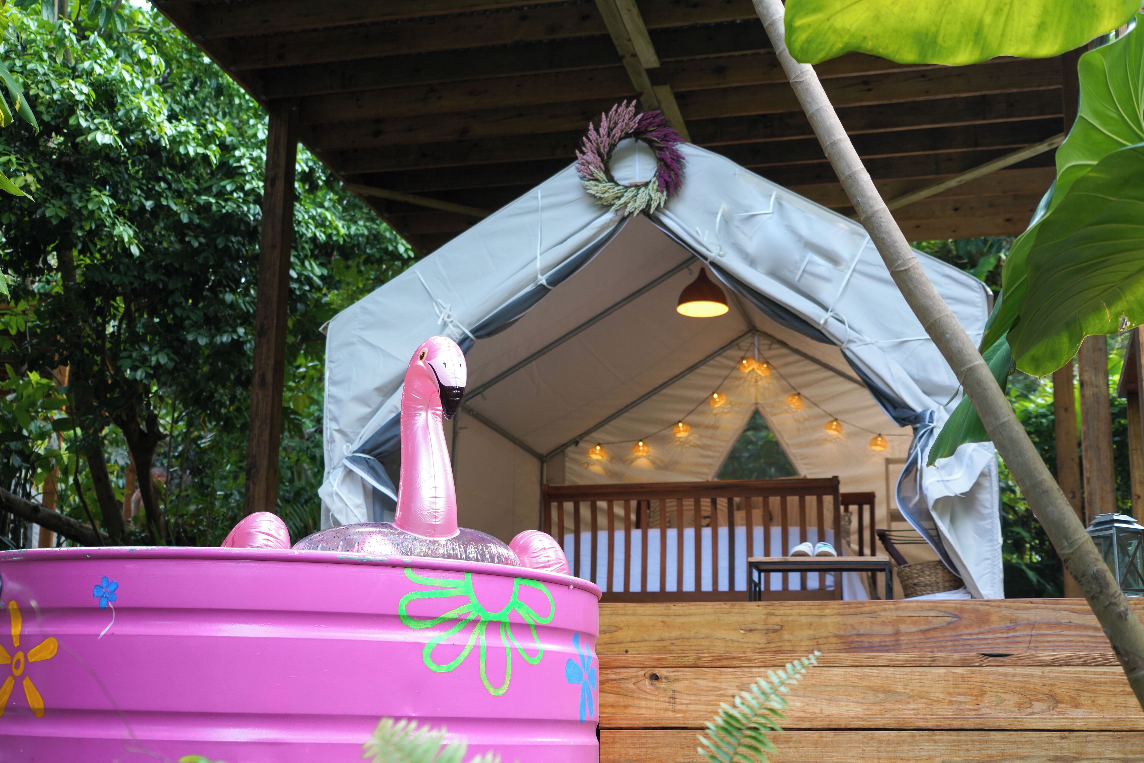 A pink barrel with a pink flamingo decoration, a white tent-like structure, and a wooden deck with a table and chairs.