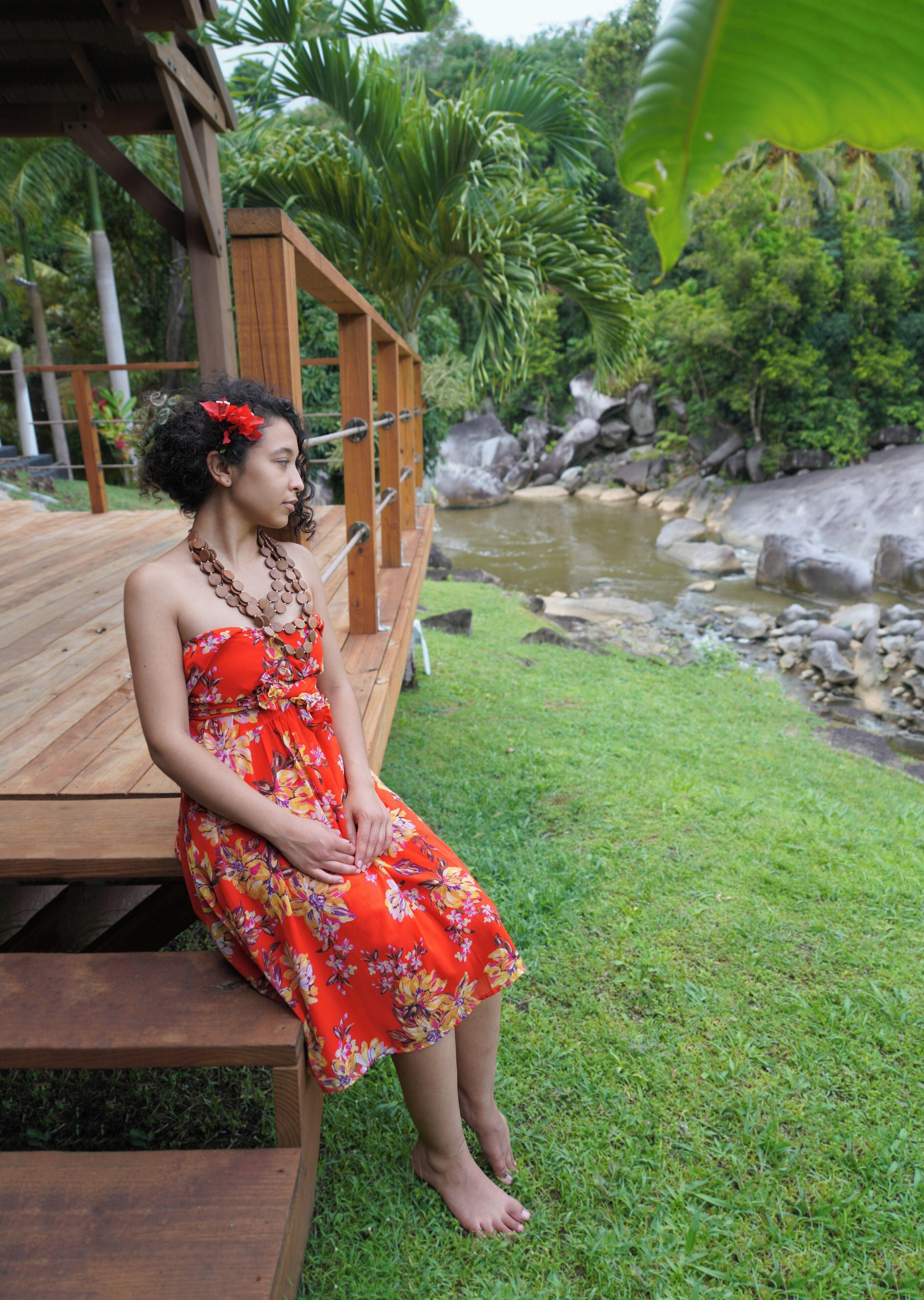 A person sitting on a wooden deck with a view of a river and greenery.
