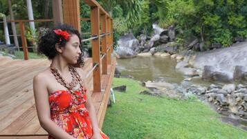 A person sitting on a wooden deck with a view of a river and greenery.