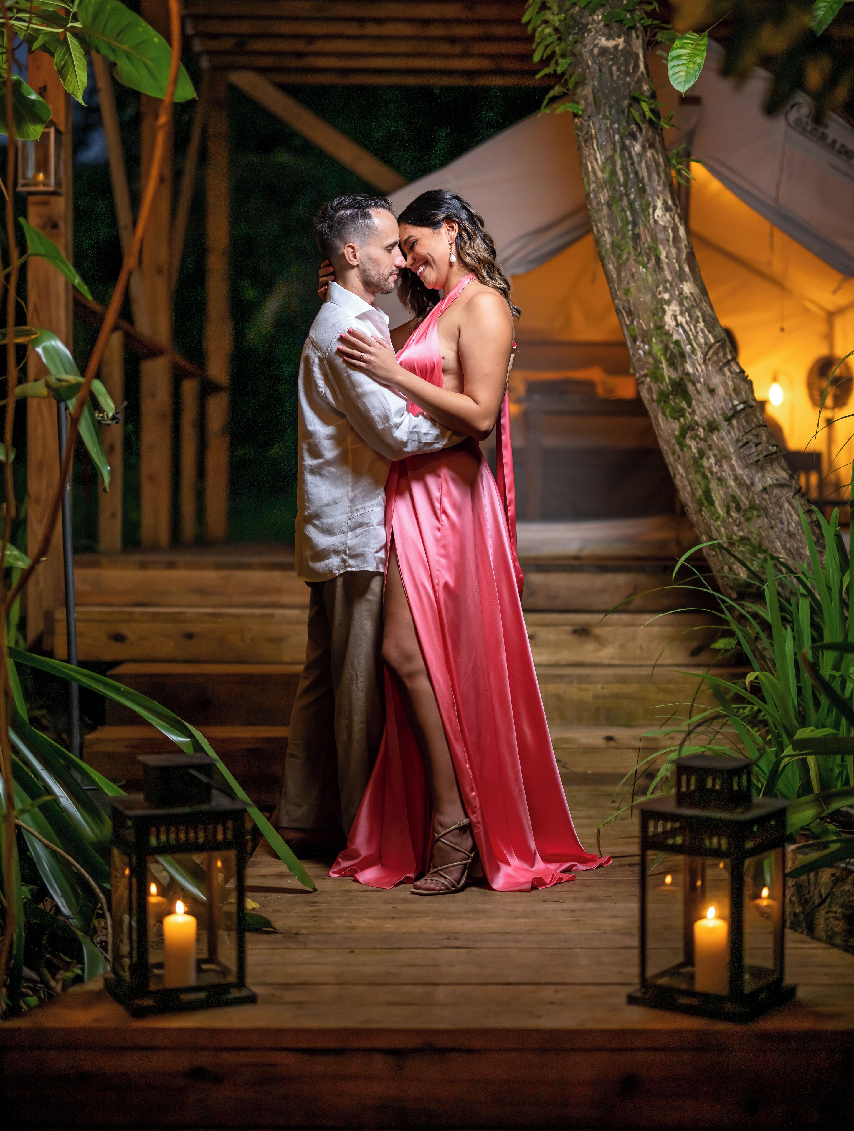 A couple embracing on a wooden deck with lanterns and greenery.