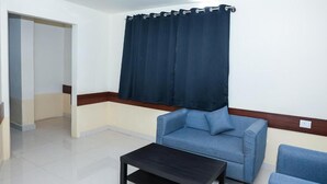 Une pièce avec un canapé bleu, une petite table et un rideau foncé.
