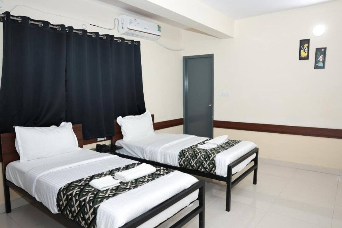 Quarto de hotel com duas camas de solteiro, uma porta e um aparelho de ar condicionado.