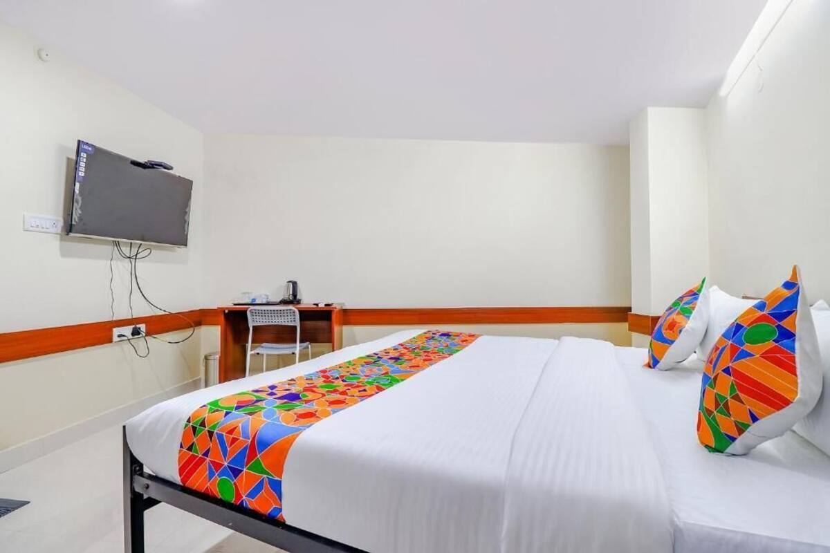 Quarto de hotel com uma cama, uma escrivaninha e uma televisão na parede.