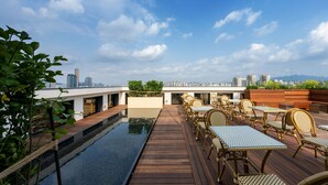 Terraza en la azotea con piscina, terraza de madera y zona de estar exterior con mesas y sillas.