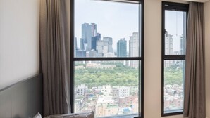 Una habitación de hotel moderna con una cama grande, un escritorio pequeño y vistas de un paisaje urbano a través de amplios ventanales.