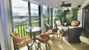 A balcony with wicker furniture, a ceiling fan, and a view of a bridge and greenery. - Riverwood Hutchinson Island (Stuart)