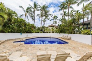 A swimming pool with lounge chairs, surrounded by palm trees and a white wall. - Kahala 414 – Ground-Floor Poipu Retreat (Koloa)