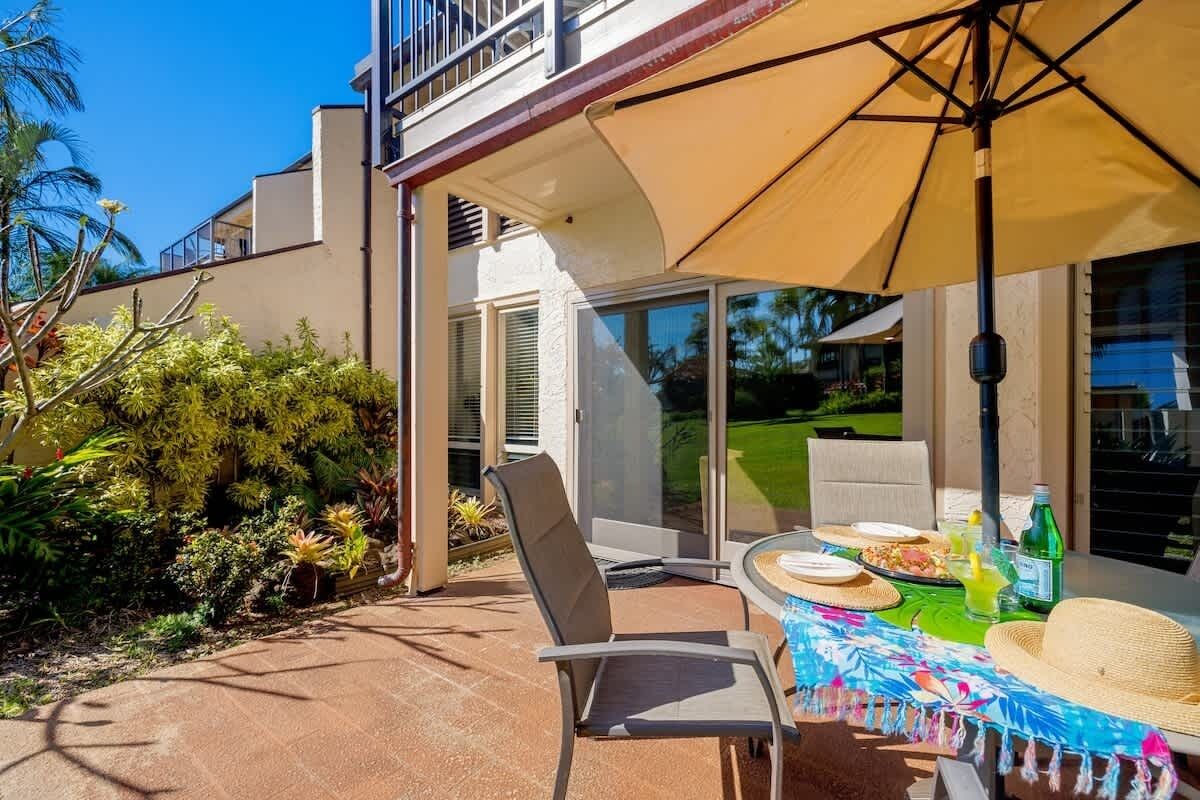 Une terrasse extérieure avec une table dressée pour le repas, une chaise et un grand parasol pour faire de l’ombre.