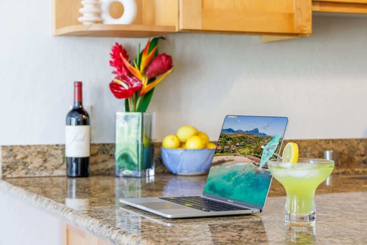 Een laptop op een aanrecht, met een fles wijn, een schaal citroenen en een cocktailglas.