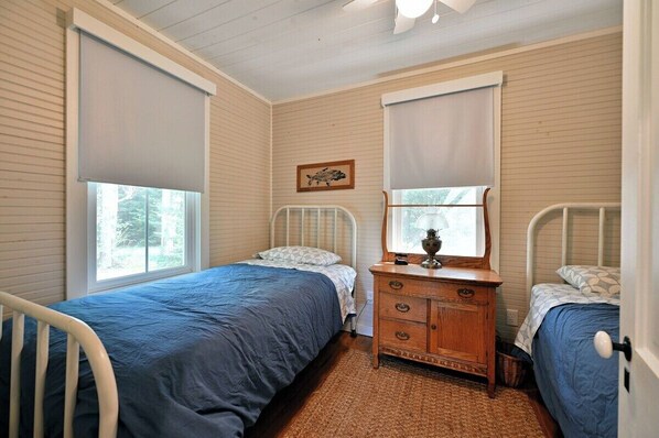 A bedroom with two single beds, a wooden dresser, and a window with a view of trees.