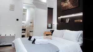 A modern hotel room with a large bed, a bedside table, a nightstand, a mirror, and a painting on the wall. - Athens Muses Suites (Athens)