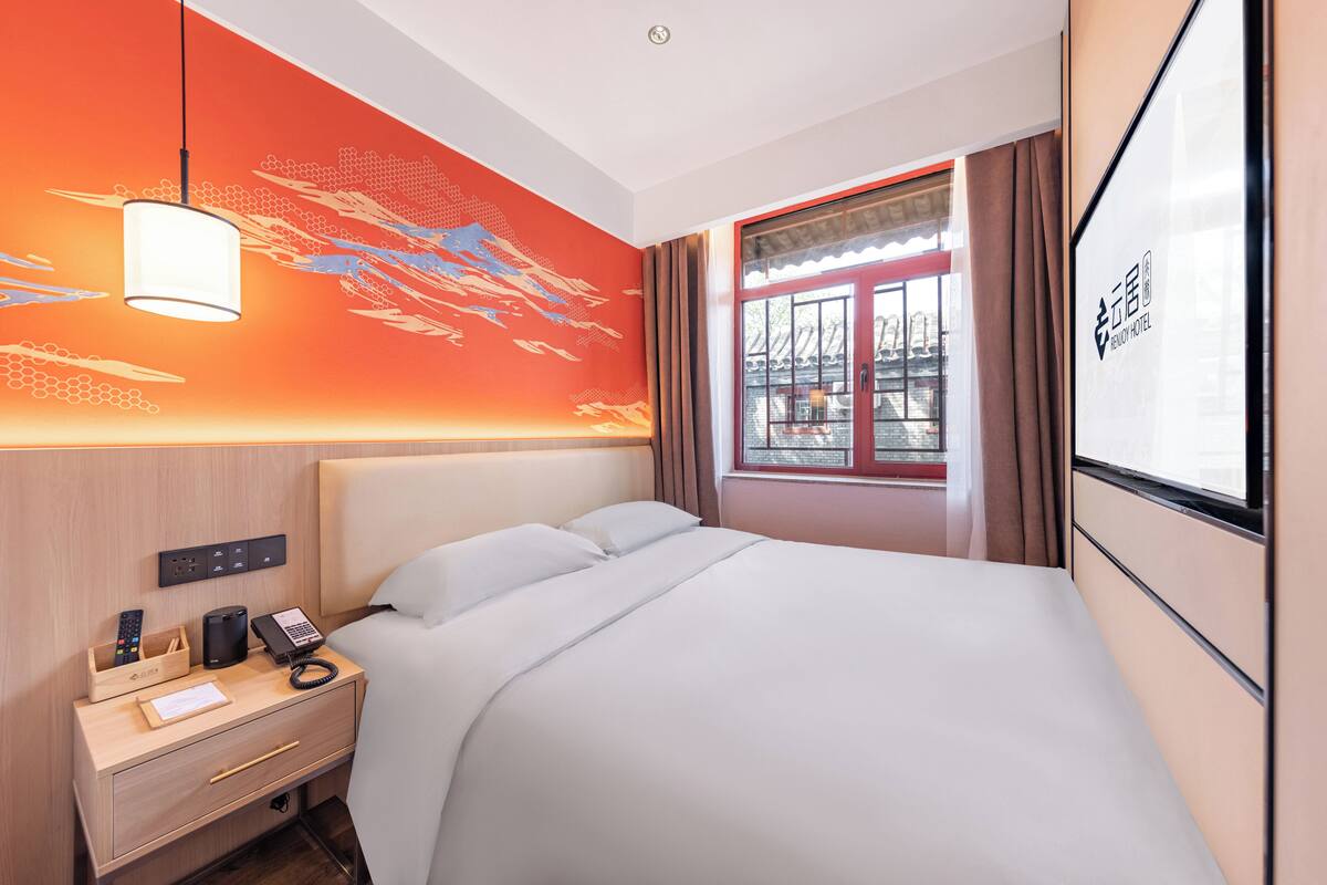 Ein Hotelzimmer mit Bett, Nachttisch, Lampe und einem Fenster mit Vorhängen.